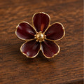 Burgundy enamel flower brooch with gold-tone center on dark wood