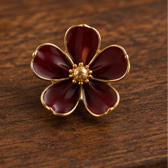 Burgundy enamel flower brooch with gold-tone center on dark wood