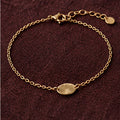 Delicate gold chain bracelet with oval charm on burgundy fabric