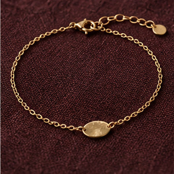 Delicate gold chain bracelet with oval charm on burgundy fabric
