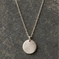 Brushed silver disc pendant necklace on charcoal stone