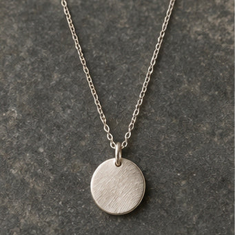 Brushed silver disc pendant necklace on charcoal stone