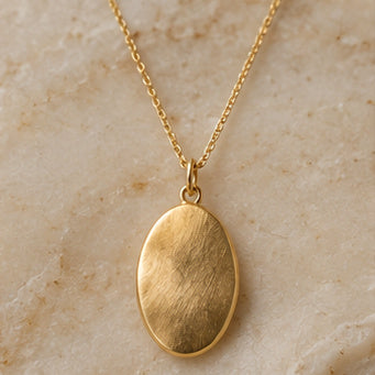 Warm gold oval pendant necklace on pale stone