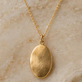 Warm gold oval pendant necklace on pale stone