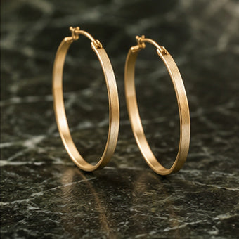 Brushed gold hoop earrings on dark green stone