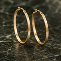 Brushed gold hoop earrings on dark green stone